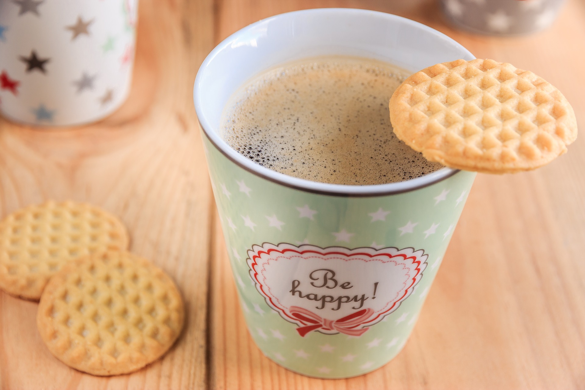 Kaffeebecher mit dem Aufdruck "be happy" und Keksen