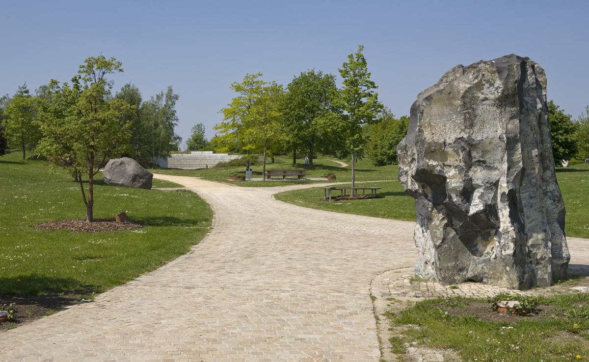 Breiter Sandweg durch Wiesen. Der Weg macht einen Bogen. Im Hinetrgrund und rechts und links sind Bäume in frühlingsgrün.