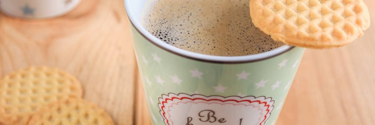 Kaffeebecher mit dem Aufdruck "be happy" und Keksen