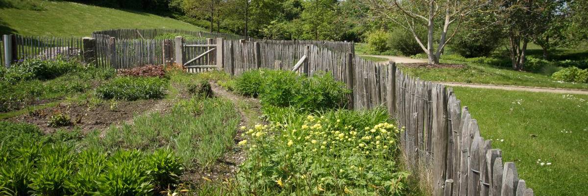 Staudenbeet im Frühling. Erste Pflanzen sind bereits zu sehen. Das ganze Beet ist mit einem Zaun eingefasst.