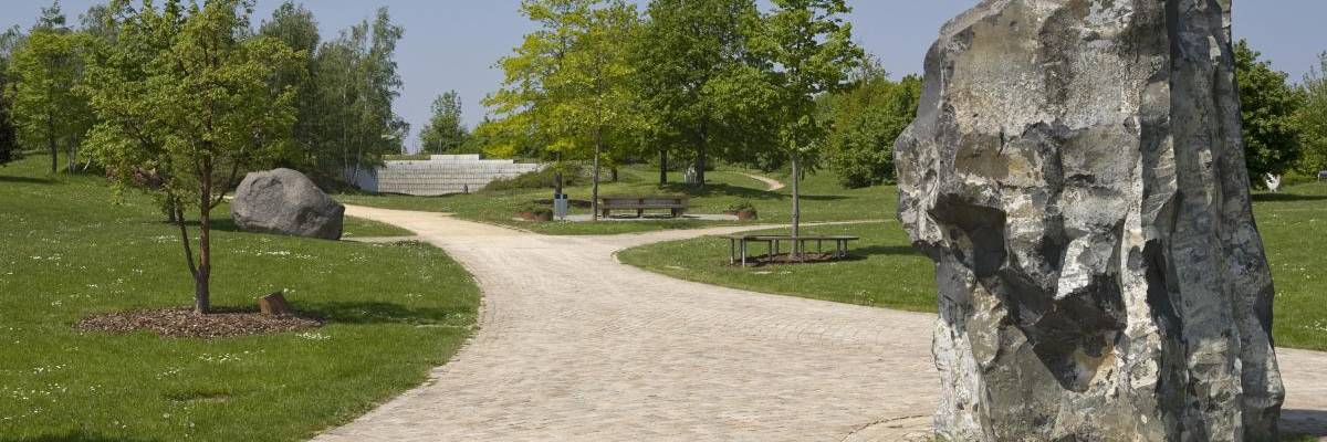 Breiter Sandweg durch Wiesen. Der Weg macht einen Bogen. Im Hinetrgrund und rechts und links sind Bäume in frühlingsgrün.