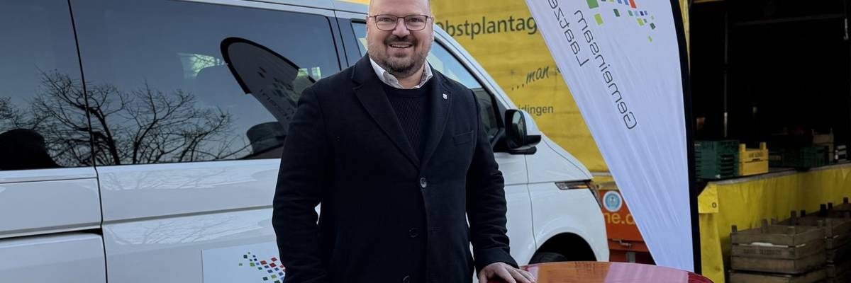 Ein Mann steht auf einem Platz neben einer Beachflag und einem Stehtisch.