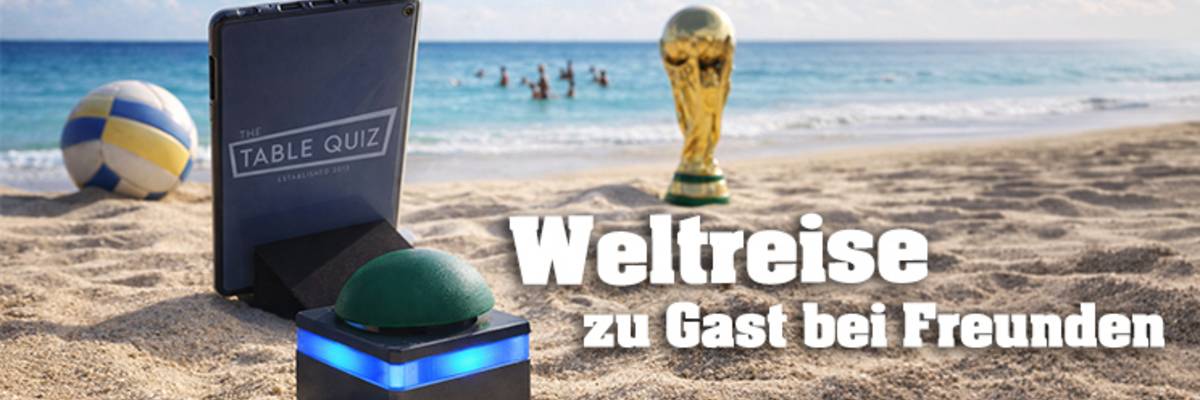 Tablet und Buzzer stehen am Strand vor dem Meer, im Hintergrund sind Menschen im Meer, ein Volleyball und der WM Pokal stehen am Strand