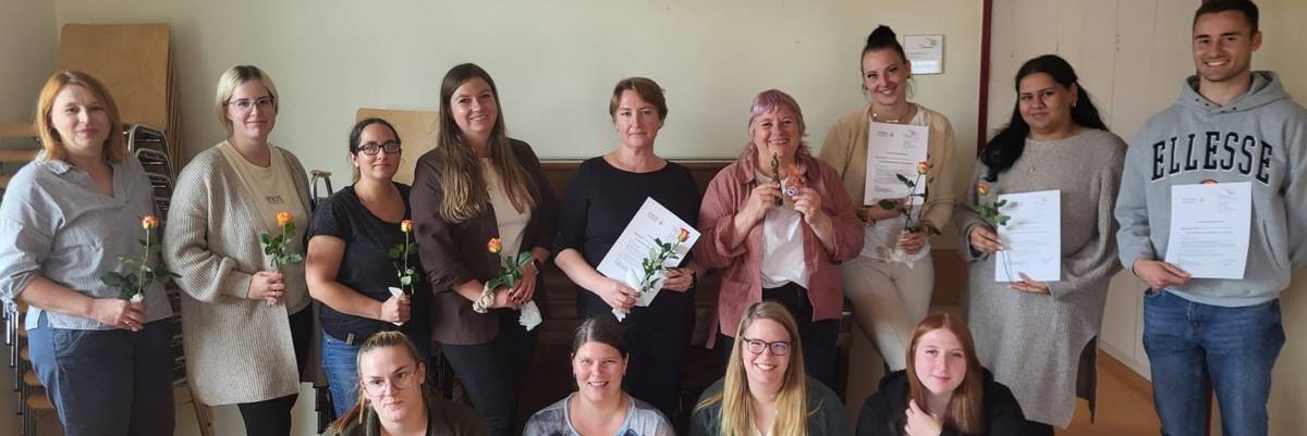 Die Teilnehmenden stehe im Halbkreis zur Kamera. Sie halten alle ihre Teilnahmebescheinigungen und eine Blume in der Hand.