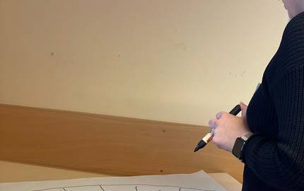 Auf einem Tisch liegt ein Vielfaltsfächer. Die päd. Fachkräfte schreiben mit einem Stift in den Fächer rein.