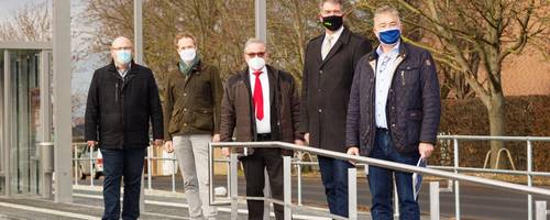 Fünf Männer stehen mit Masken auf einem Bahnsteig