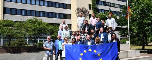Eine Gruppe von Menschen steht auf einem Platz. Sie halten eine Europaflagge.