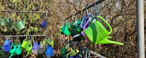An einer Eisenstange sind bunte Gießkannen mit Schlössern befestigt.