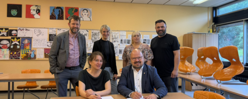 Bürgermeister Kai Eggert und Planerin Kristina Gronau unterzeichnen in einem Klassenraum den Vertrag zur Sanierung des C-Trakts der Albert-Einstein-Schule. Hinter ihnen stehen weitere Vertreterinnen und Vertreter von Schule und Stadtverwaltung.