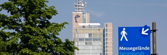 Laubbaum, Bürogebaude der deutschen Messe AG und ein blaues Hinweisschild zum Messegelände
