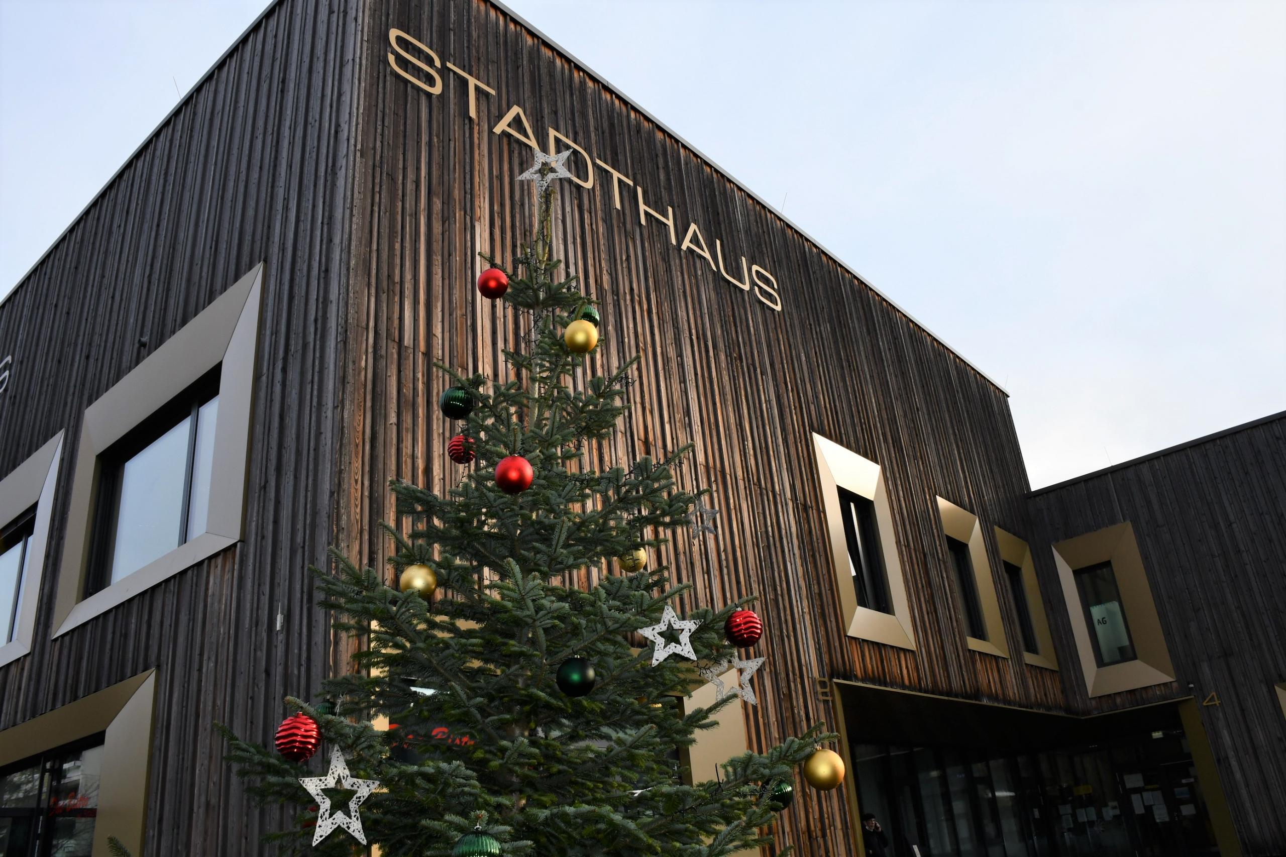 Ein Weihnachtsbaum, der mit roten und goldenen Kugeln geschmückt ist, steht vor einer Holzfassade.