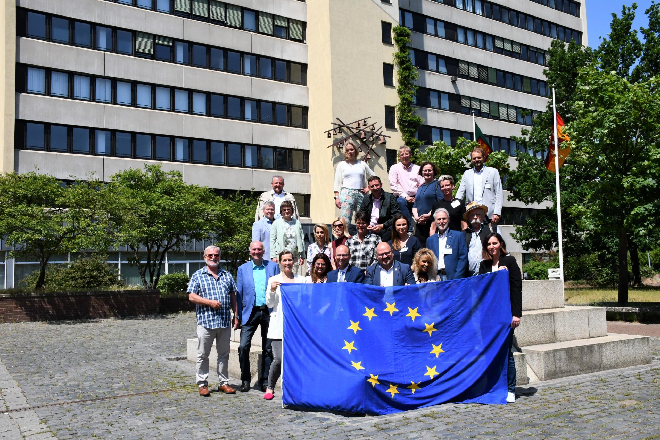 Eine Gruppe von Menschen steht auf einem Platz. Sie halten eine Europaflagge.