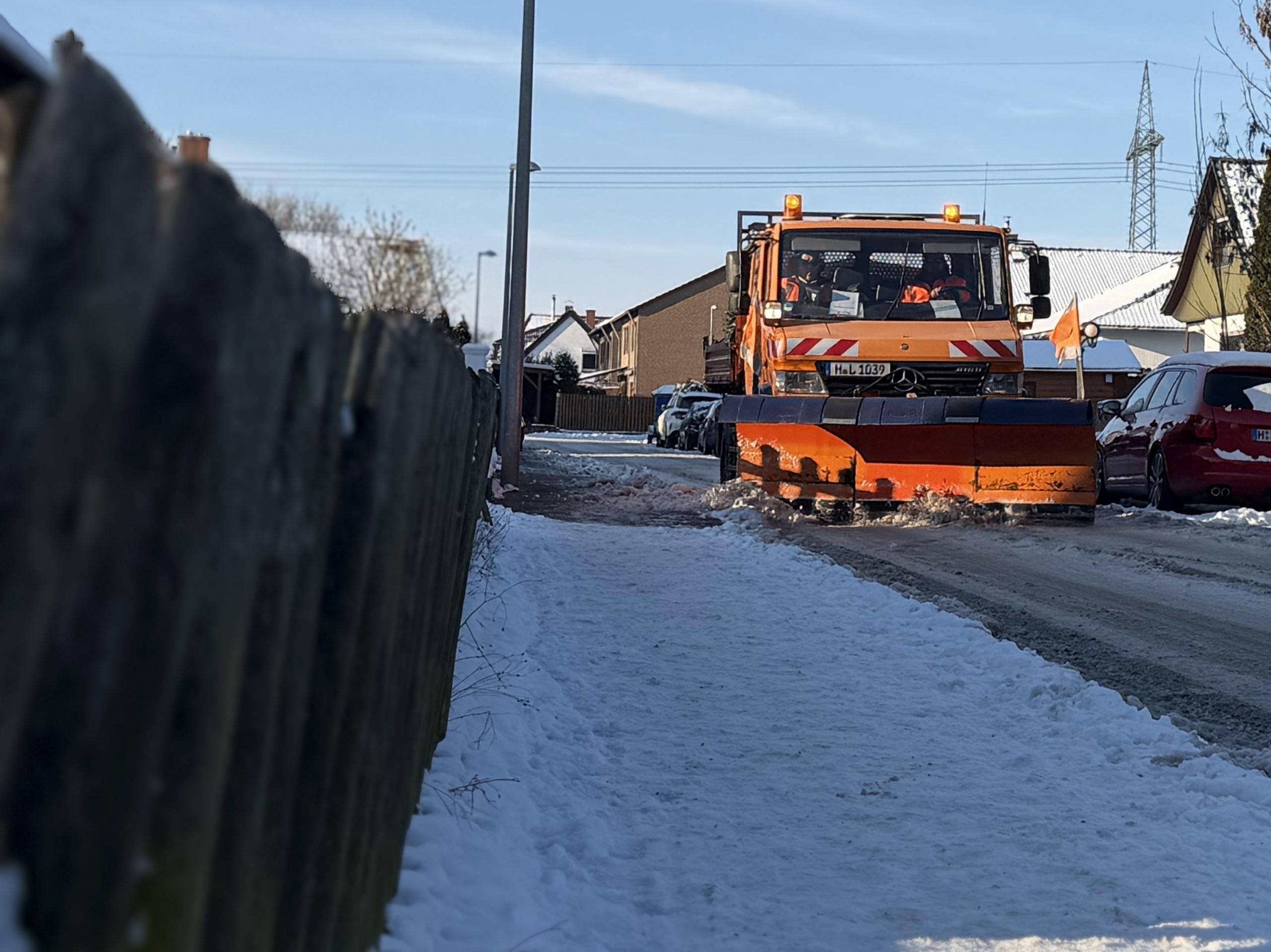 Ein LKW mit einem Schneeschild schiebt Schnee auf einer verschneiten Fahrbahn zur Seite.