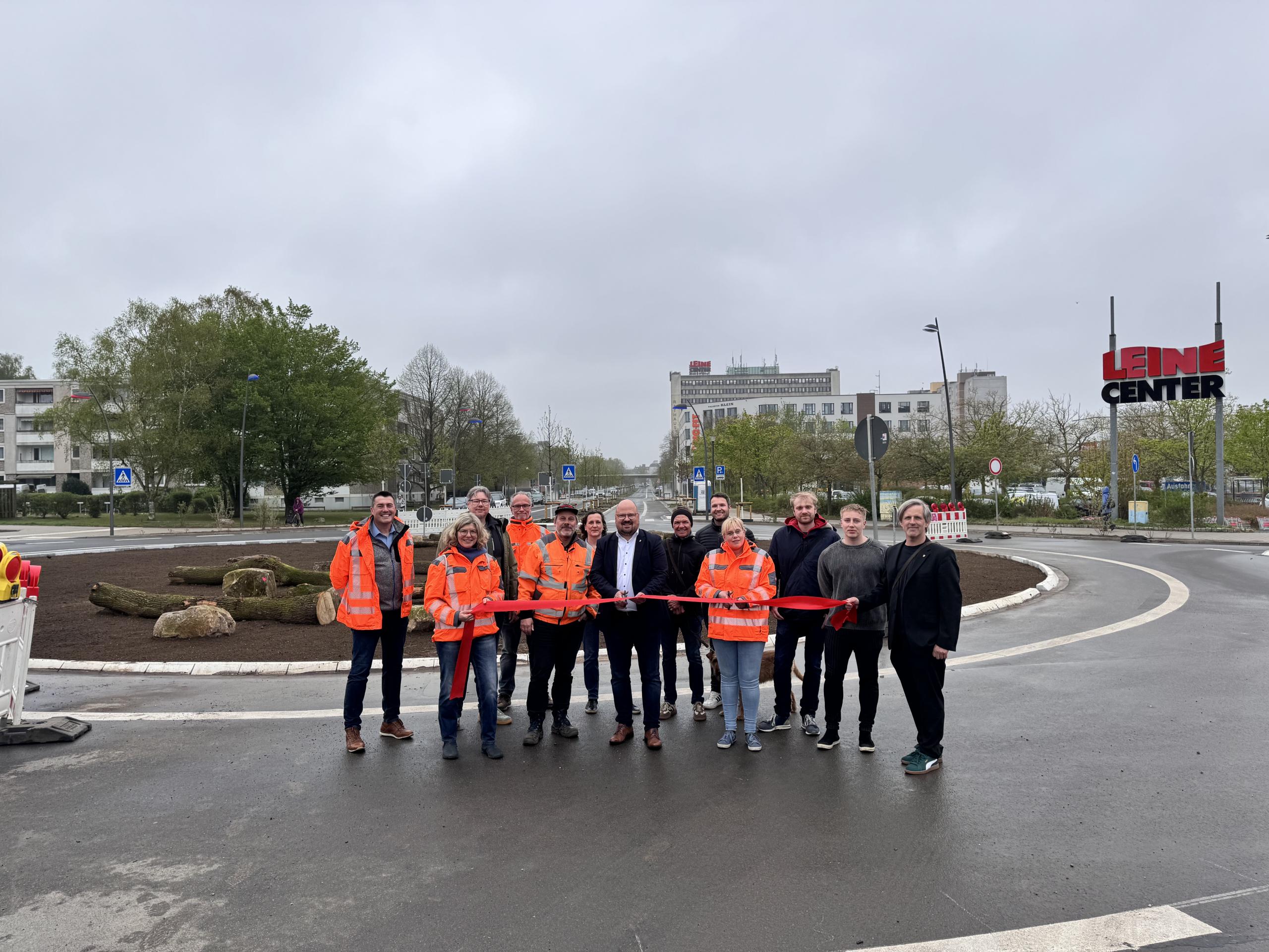 Eine Gruppe Menschen steht an einem Kreisverkehr und hält ein rotes Band.