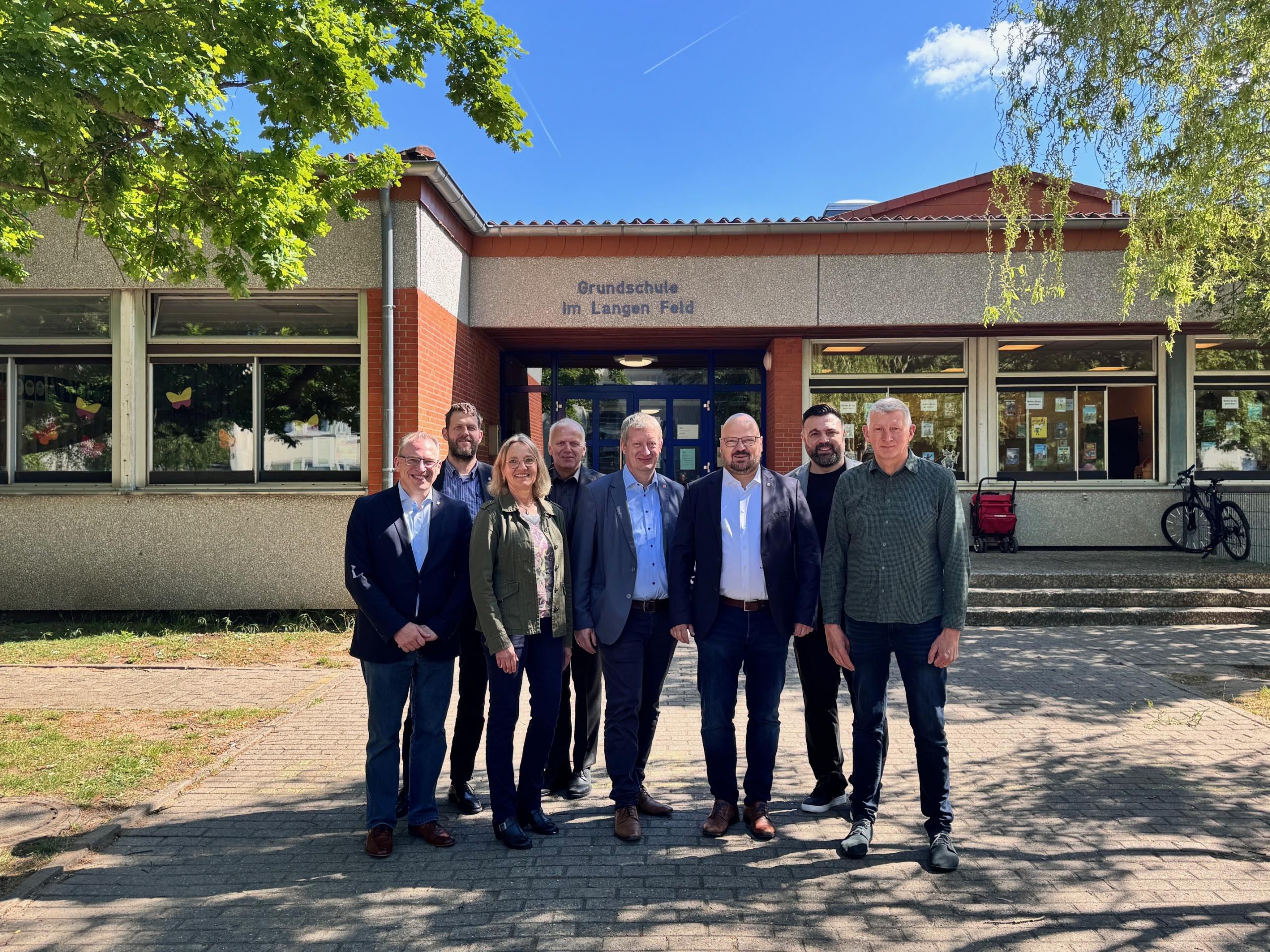 Eine Gruppe Menschen steht vor einem Schulgebäude.