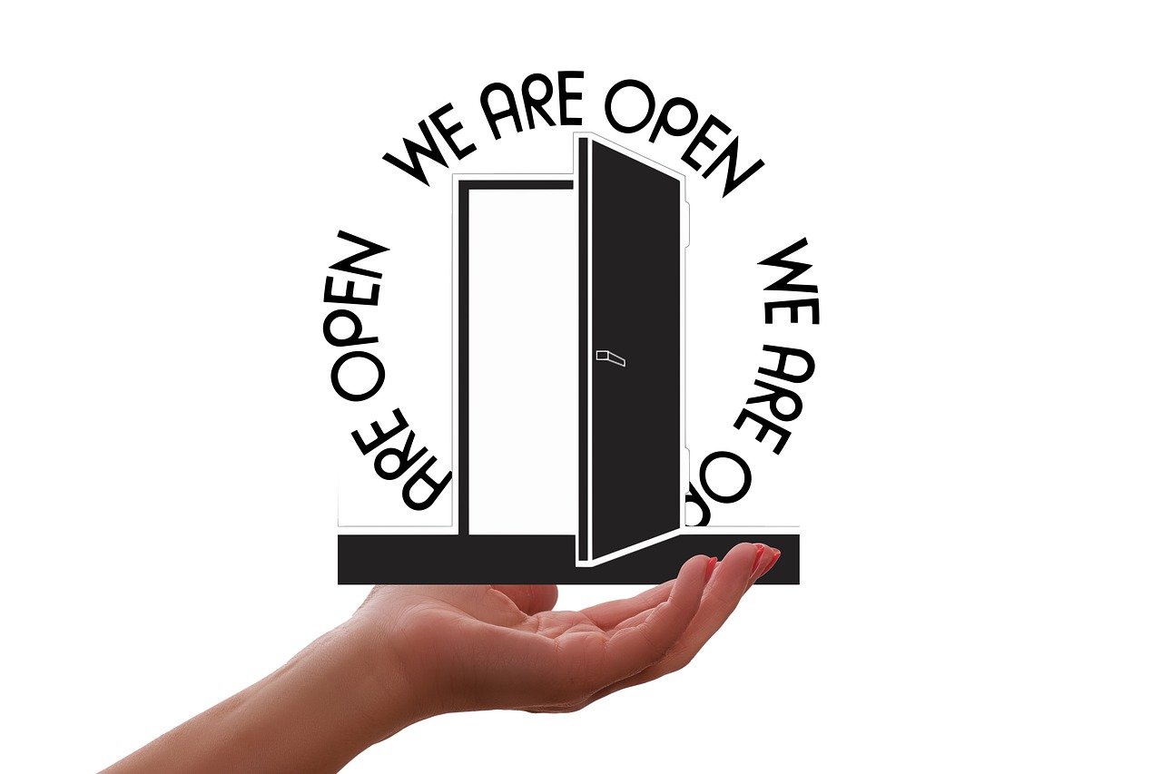 Piktogramm einer offenen Tür, die von einer Hand gehalten wird. Der Schriftzug We are open ist kreisförmig darum gestaltet.
