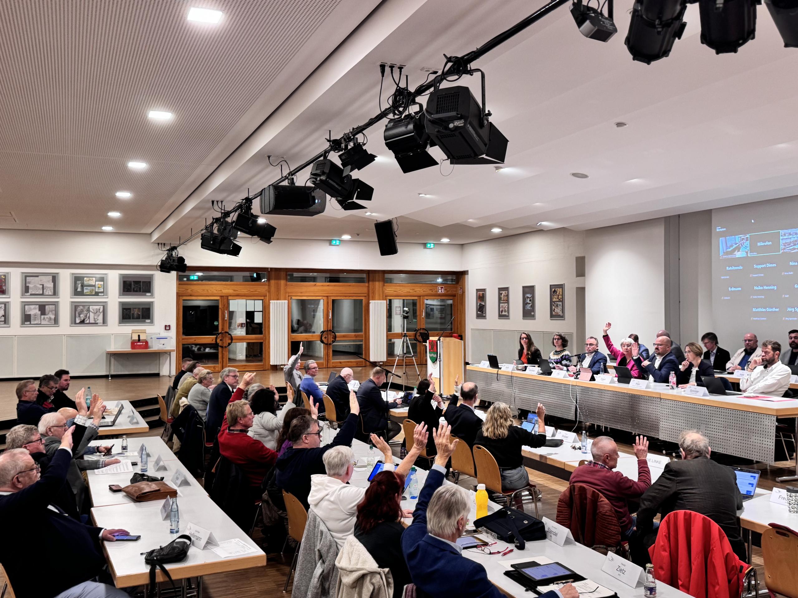 Menschen an Tischen heben die Hände zur Abstimmung.