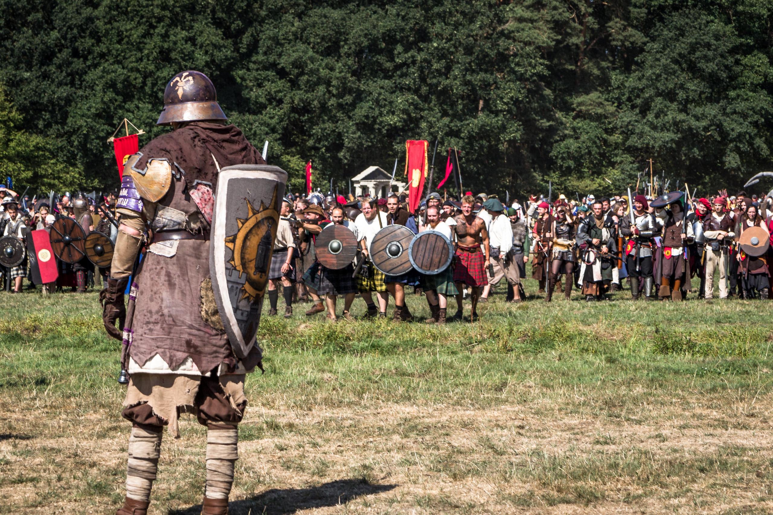 Mittelalterlich verkleideter Kämpfer steht mit einem Schild bewaffnet einer Gruppe auf einem Feld gegenüber