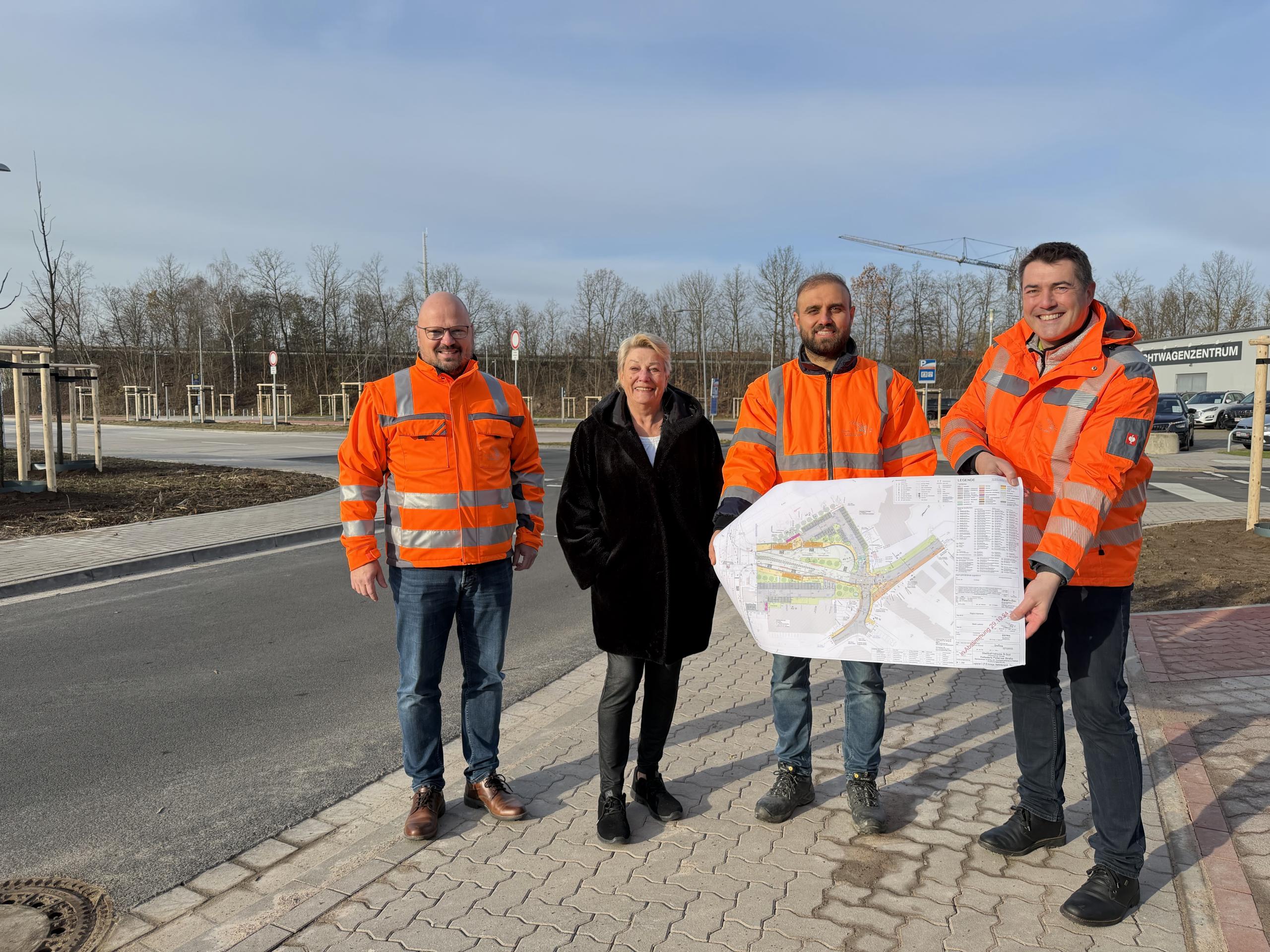 Freuen sich über die Fertigstellung: Laatzens Bürgermeister Kai Eggert, Rethens stellv. Ortsbürgermeisterin Hannelore Flebbe mit Burhan Al Khalaf und Olaf Klaus-Pohl vom Team Tiefbau der Stadt Laatzen. ©Stadt Laatzen Drei Männer in orangenen Warnjacken und eine Frau stehen an der Einmündung einer neuen Straße auf dem Gehweg.
