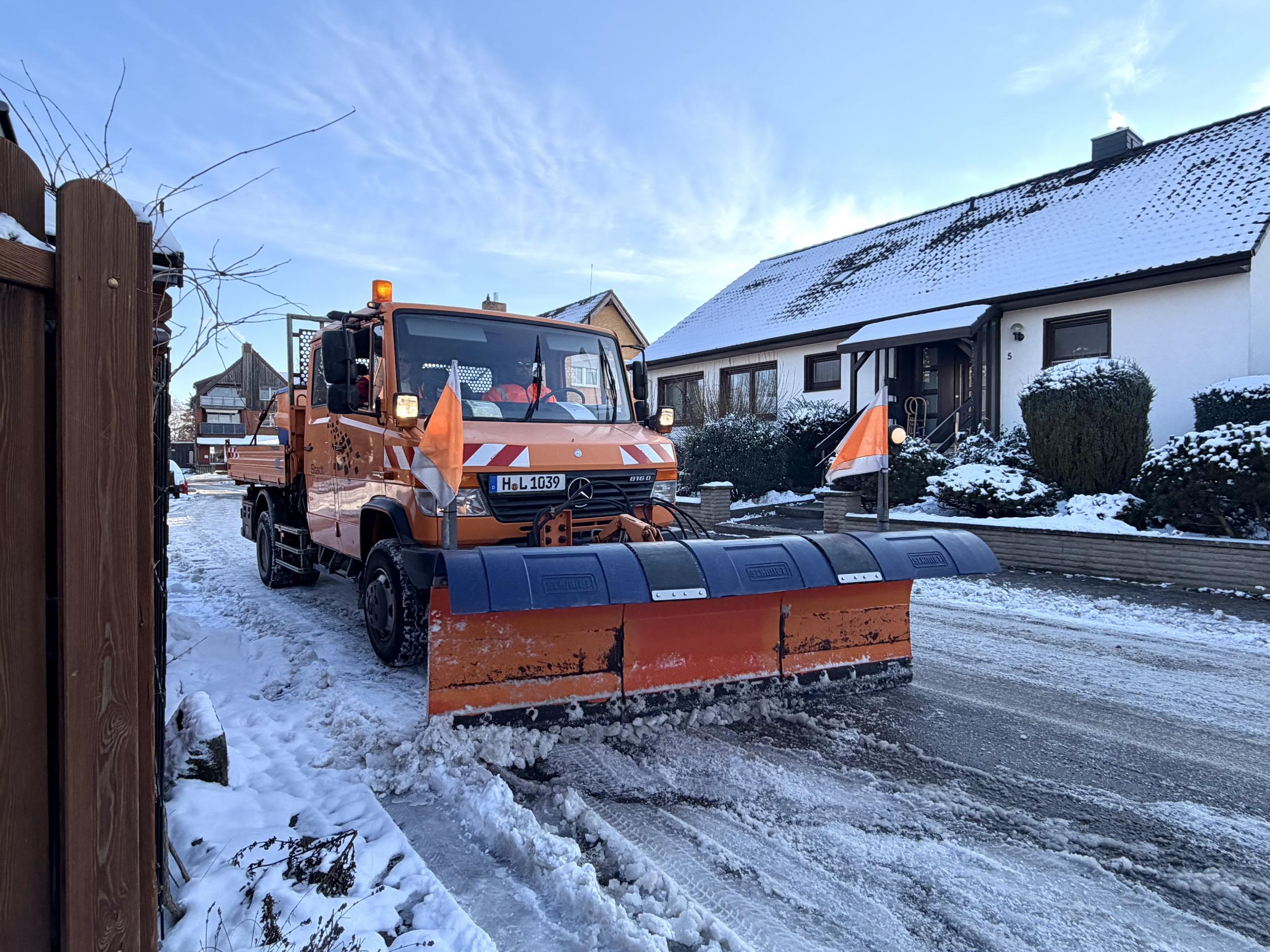 Ein Räumfahrzeug mit breitem Schneeschild fährt über eine verschneite Straße.
