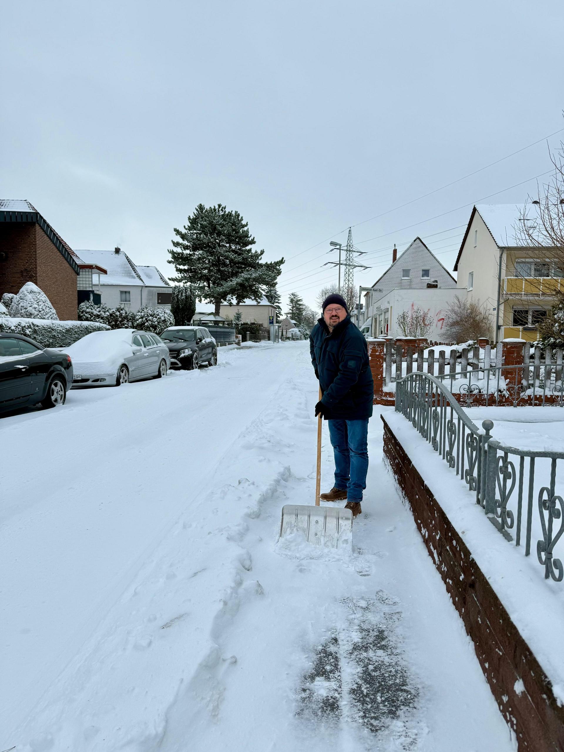 Bürgermeister Kai Eggert räumt mit dem Schneeschieber vor einem Grundstück.
