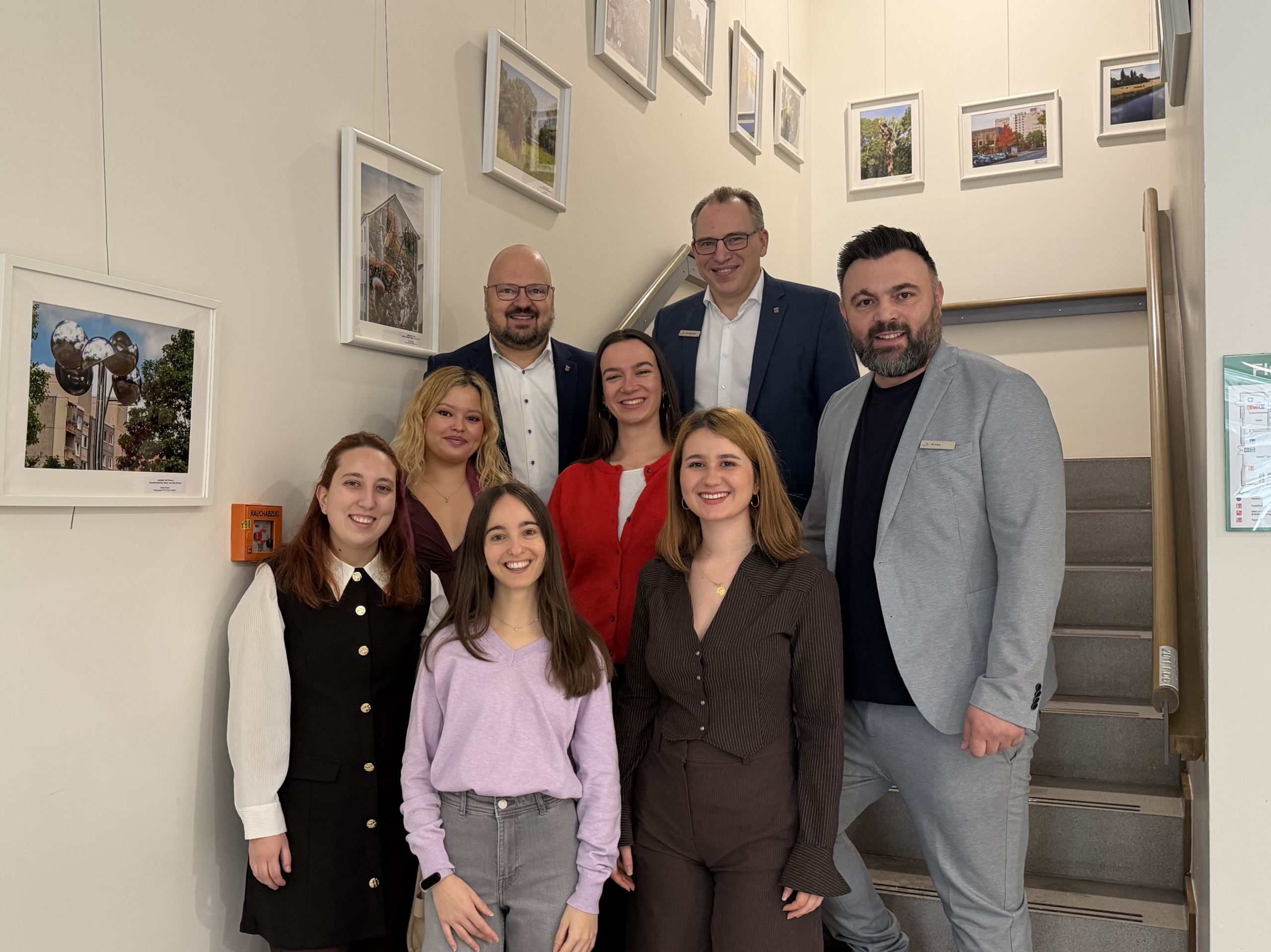 Fünf Frauen stehen neben drei Männern auf einer Treppe. Alle lächeln in die Kamera.