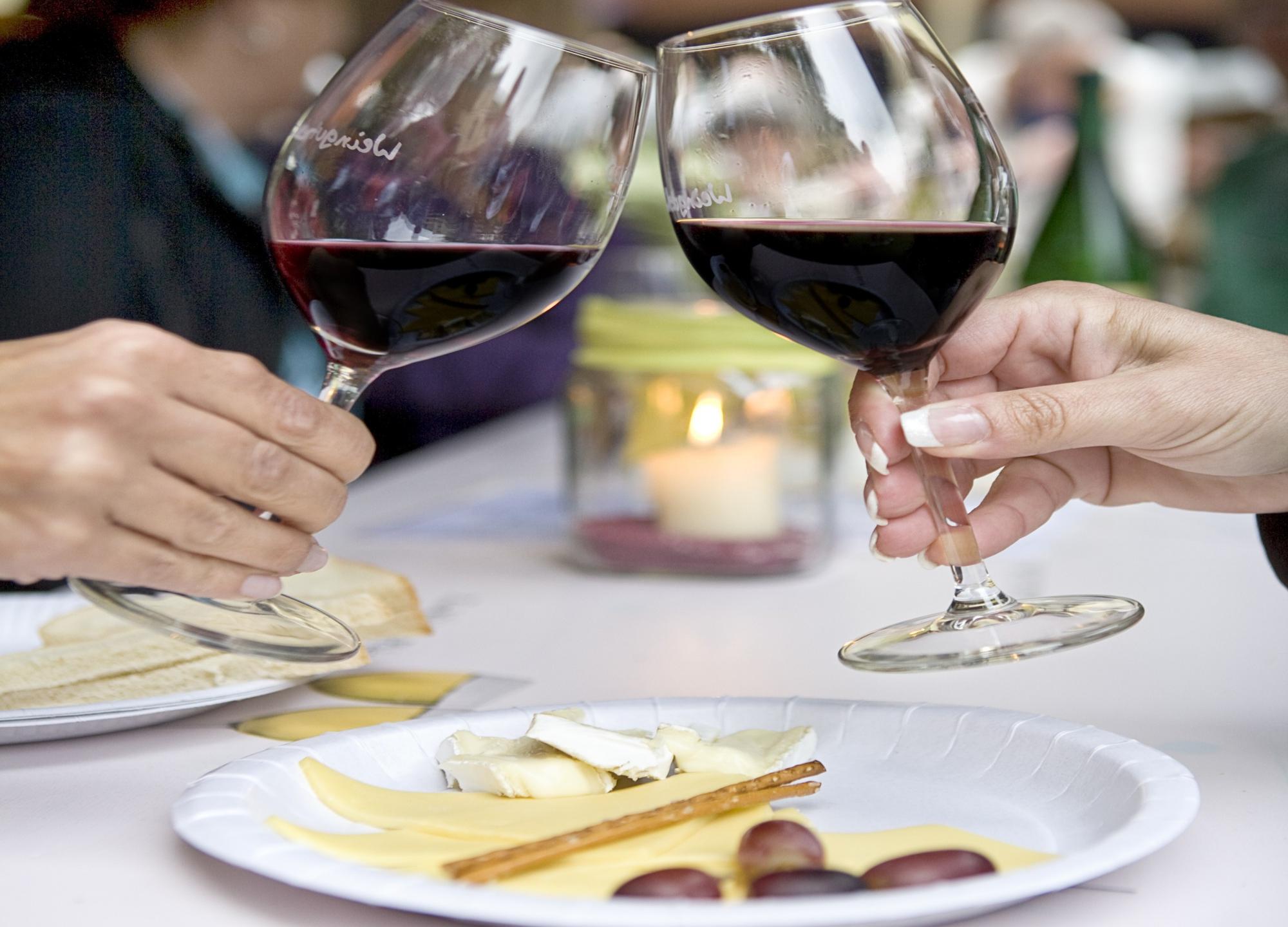 zuprostende Gläser mit Rotwein und Käseplatte im Vordergrund
