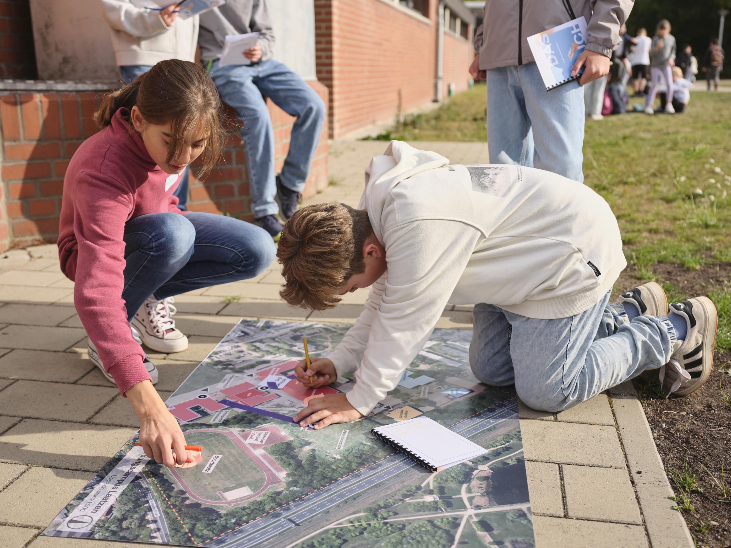 Zwei Kinder tragen Informationen auf einen Lageplan eines Schulgeländes zusammen