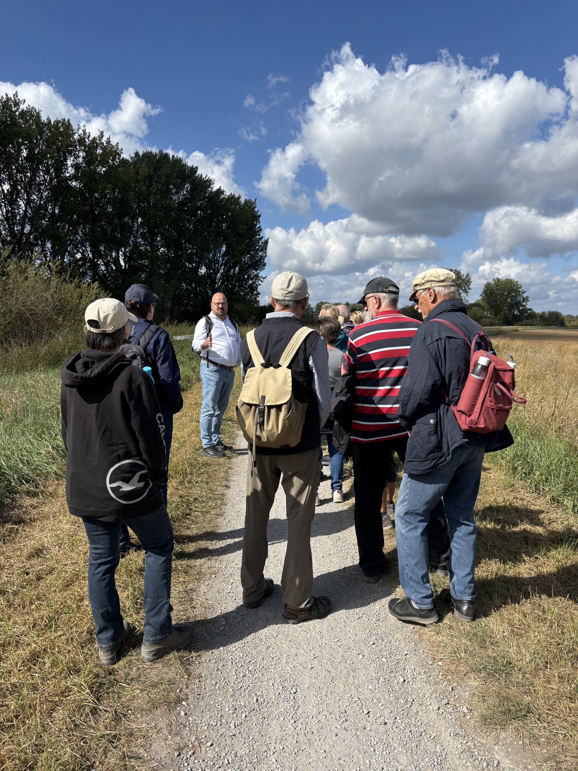 Bürgermeister Kai Eggert spricht auf einem Feldweg zu Personen, die Rucksäcke tragen.