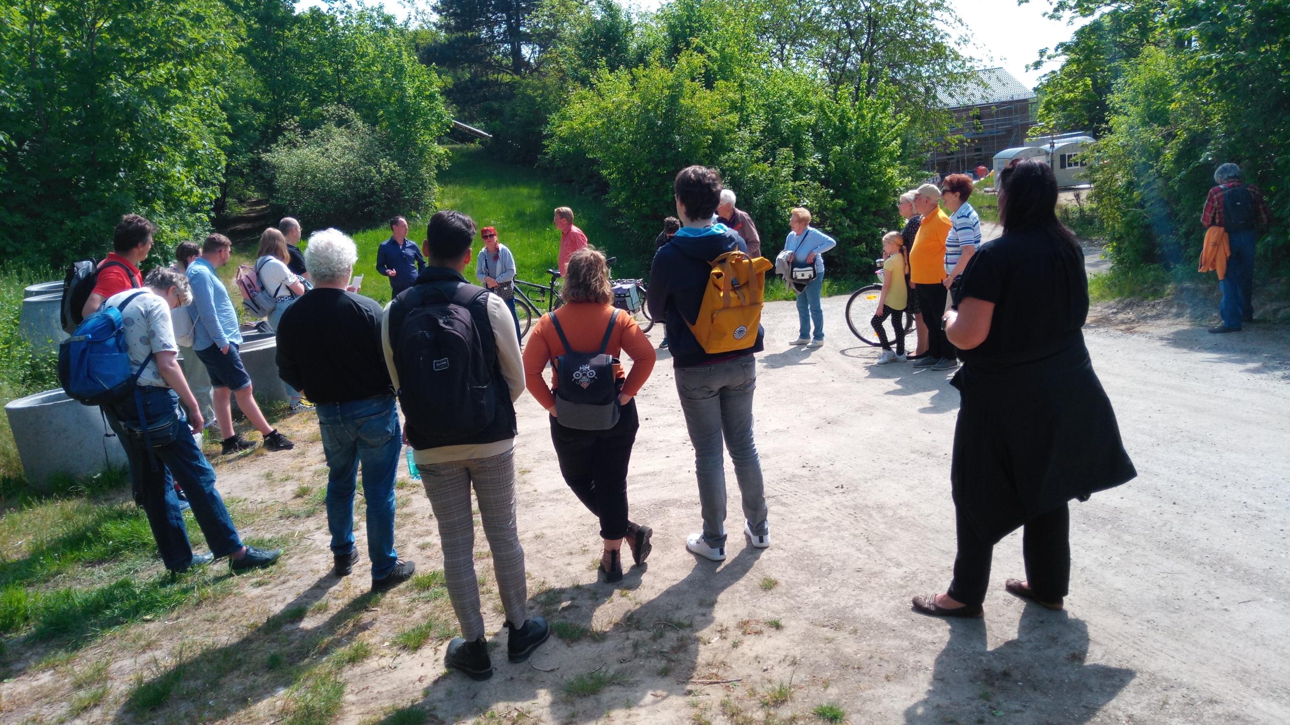 Eine Gruppe von Personen stehend im Kreis, die sich unterhalten. Im Hintergrund grüne Büsche und Gras.