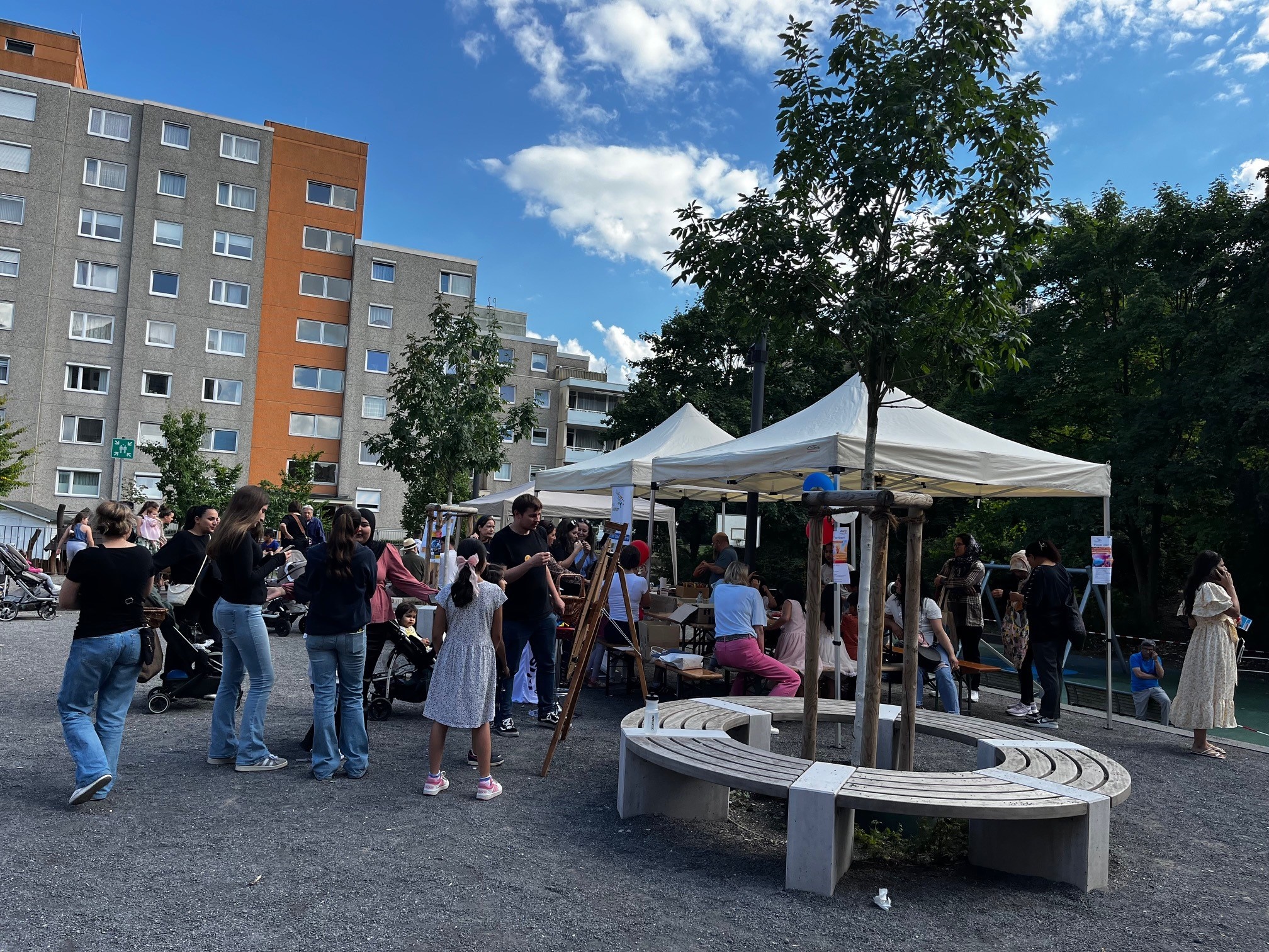 Viele Personen auf einem Fest. Pavillons mit Aktionen zur Teilnahme. Hochhäuser im Hintergrund.