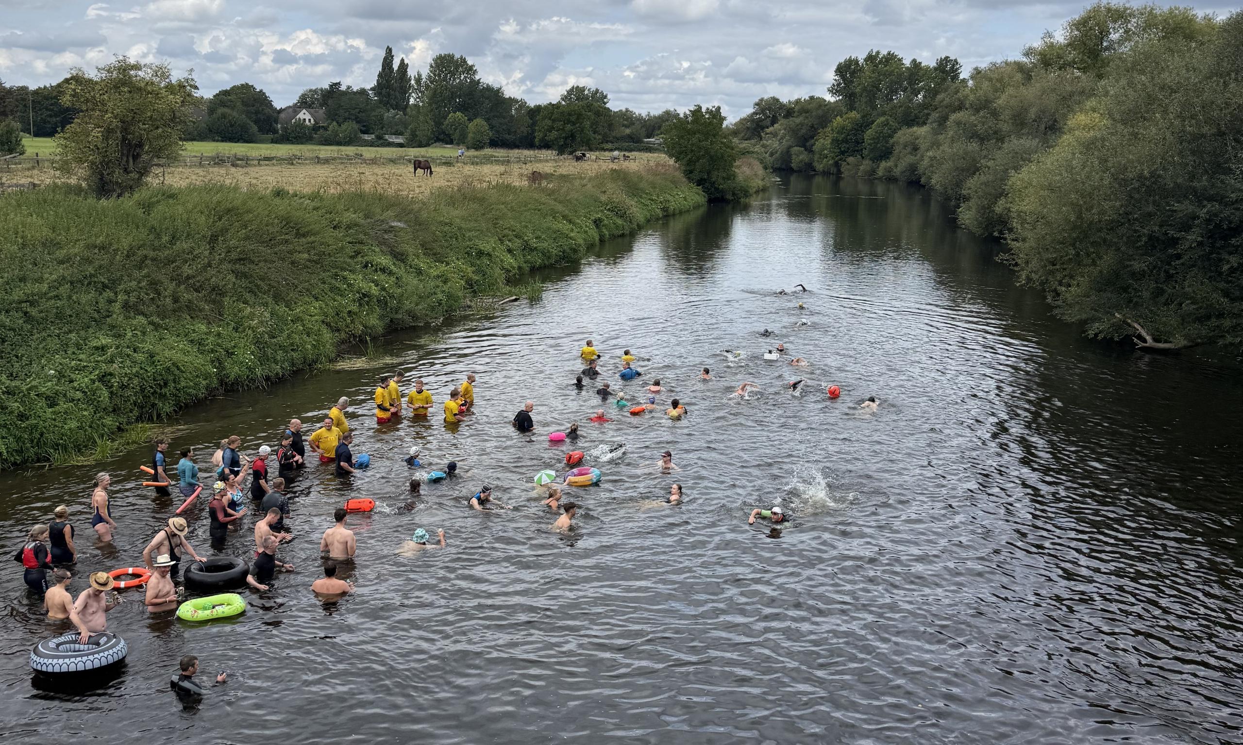 Schwimmerinnen und Schwimmer befinden sich in einem Fluss. Sie sind von oben, von einer Brücke aus fotografiert worden.