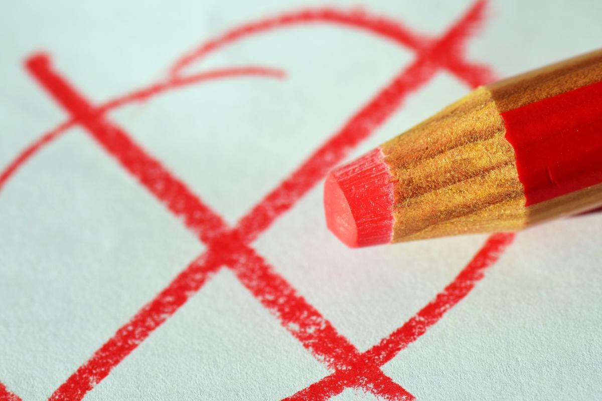 Roter Stift der ein rotes Kreuz gemalt hat. Dieses ist im Hintergund zu sehen.