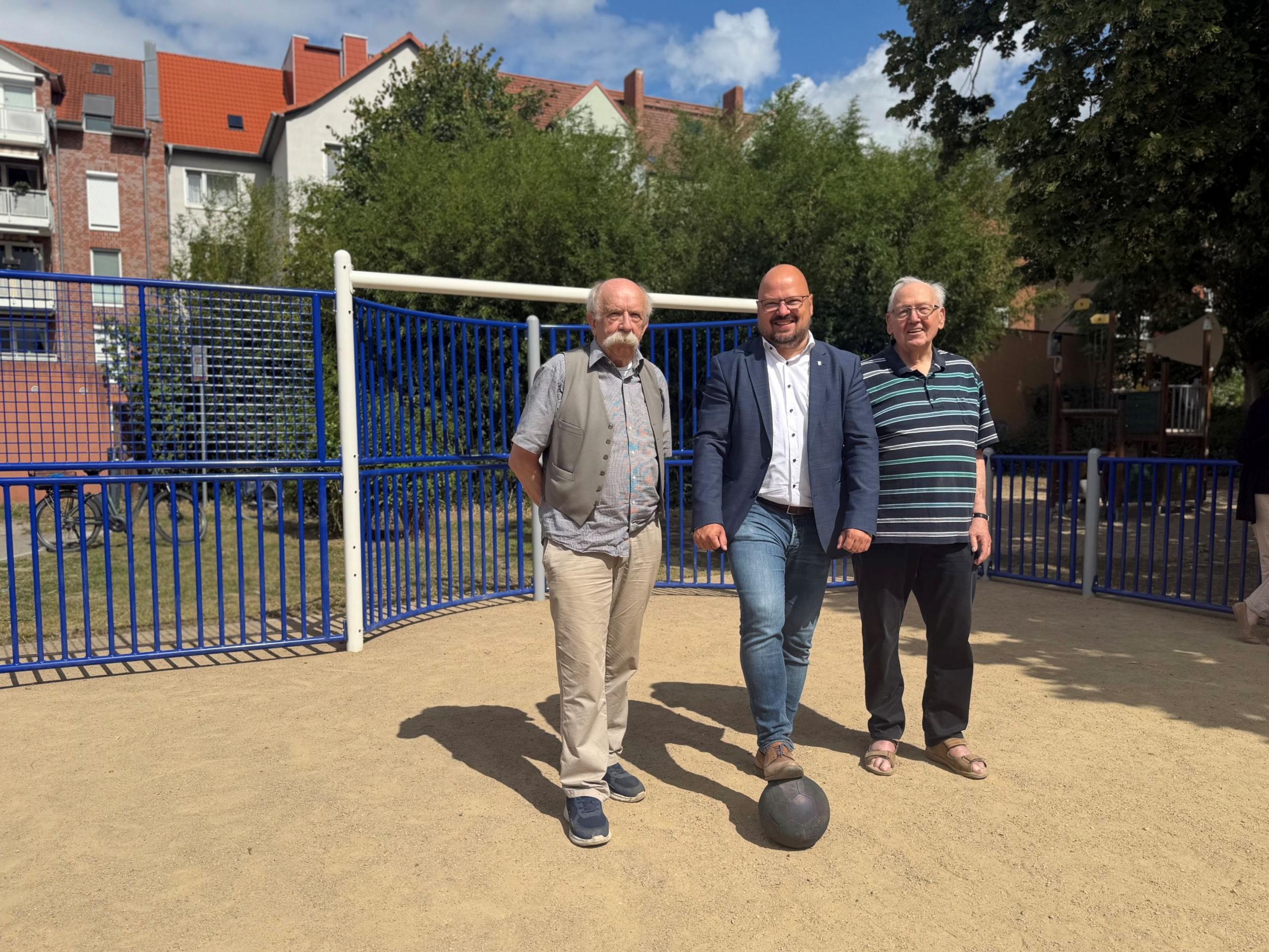 Vom Parkplatz zur Bolzfläche: Bürgermeister Kai Eggert (mittig), Ortsbürgermeister Bernd Stuckenberg (r.) und dessen Stellvertreter Siegfried Guder eröffneten den neuen Fußballkäfig am Kreuzweg. ©Stadt Laatzen Drei Männer stehen vor einem blauen Fußballtor aus blauem Metall.