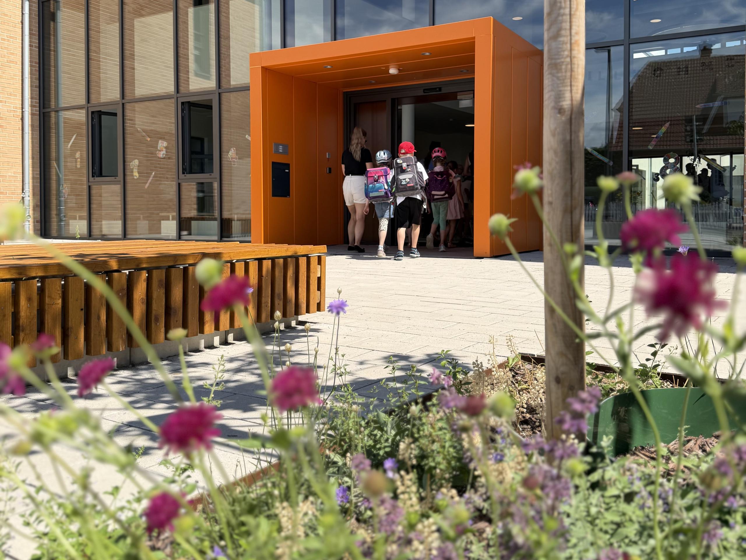 (Symbolbild): 3 von 4 Grundschulkinder aus Laatzen besuchen nach den Sommerferien den offenen Ganztag. ©Stadt Laatzen Grundschülerinnen und -schüler betreten mit Schulranzen auf dem Rücken einen orangenen Eingangsbereich einer Schule.
