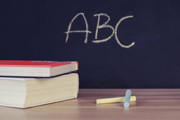 Auf einer Tafel stehen die Buchstaben ABC geschrieben. Im Vordergrund liegen Bücher und Kreide