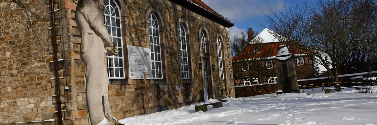 Blick auf eine Kirche. Im Vorgergrund eine Skulptur.