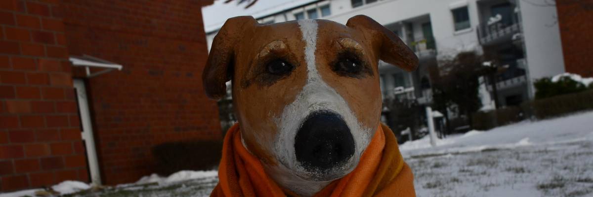 Hundeskulpur mit Schal auf einer verschneiten Grünfläche