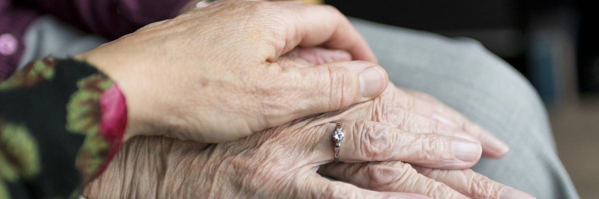 Junge Hand liegt schützend über der Hand einer älteren Person