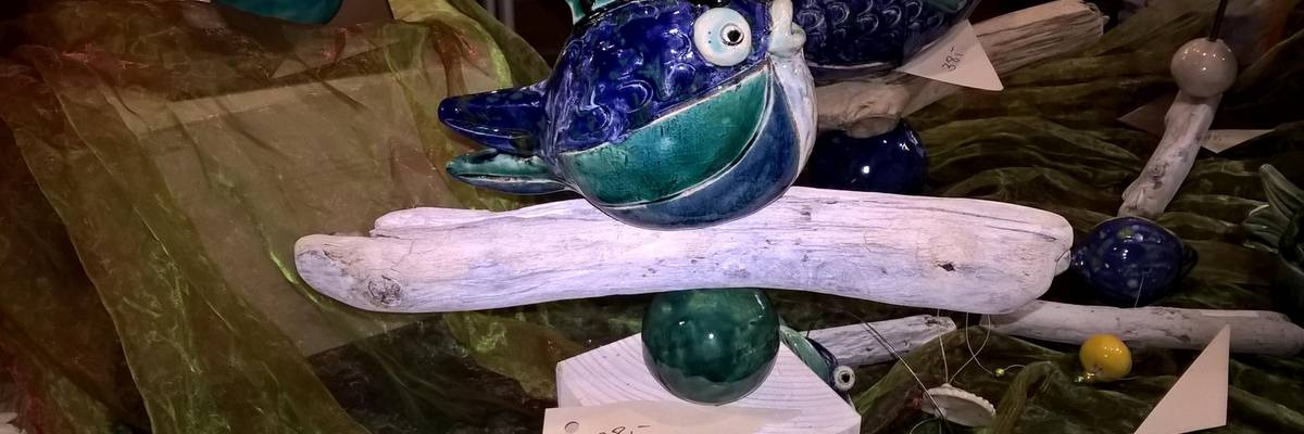 Ein Fischkunstwerk welches auf einem Block, einer Kugel und einem Stück Holz sitzt.