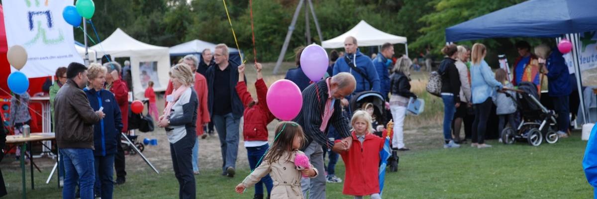 Menschengruppe mit tanzenden Kindern und Ballons im Vordergrund