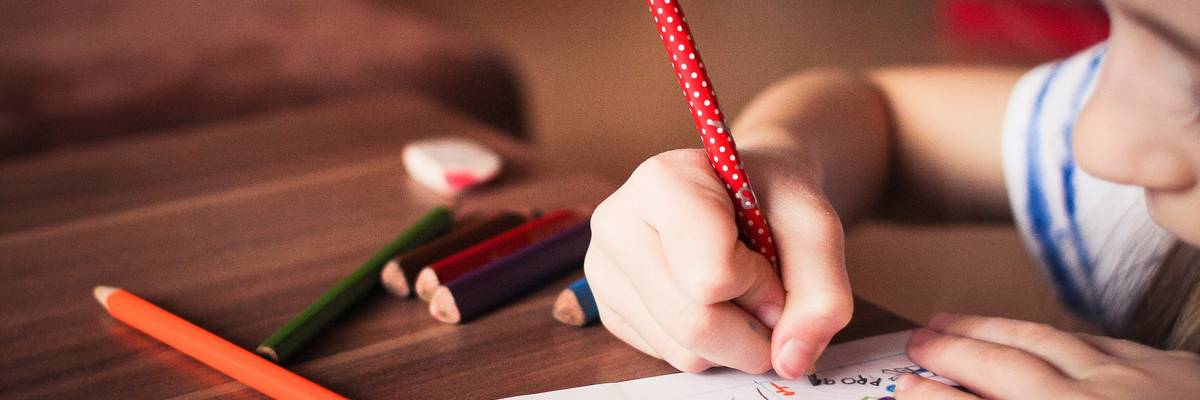 Ein Mädchen sitzt an einem Tisch. In der Hand hält sie einen Bleistift und füllt ein Arbeitsblatt aus.