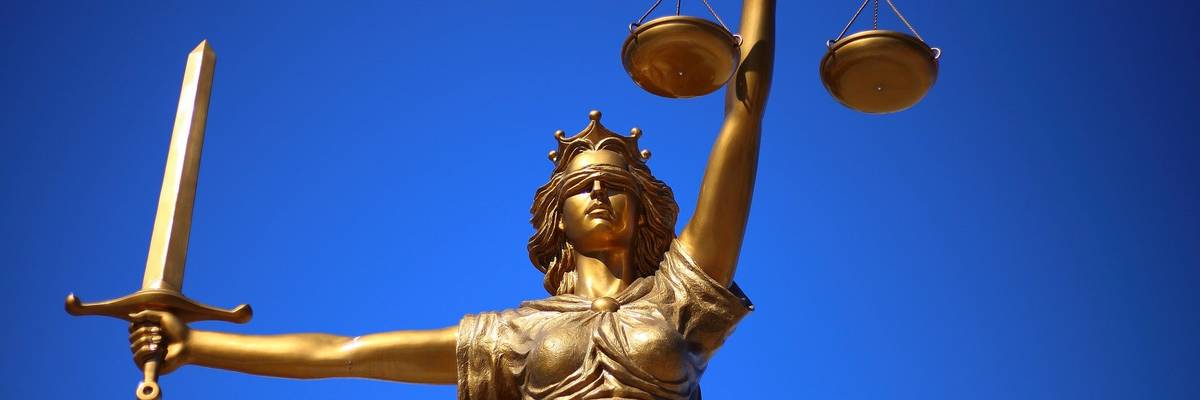 Statue einer Justizia vor einem blauen Himmel.
