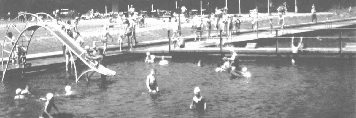 Schwarz weiß Fotografie mehrerer Schwimmbecken, in denen sich zahlreiche Schwimmer aufhalten.