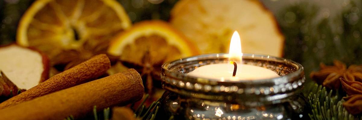 Kerze auf Weihnachtsgesteck mit Zimtstangen und Organgenscheiben