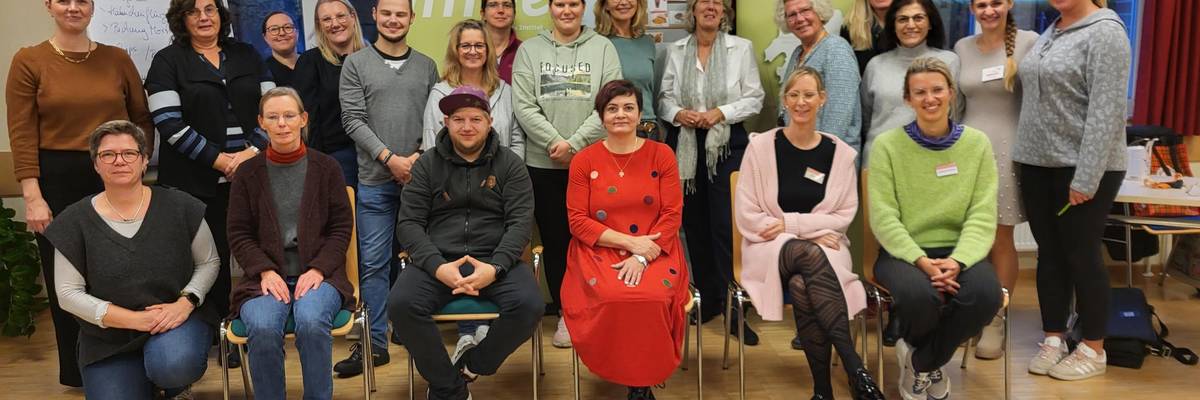 Eine Gruppe Frauen sitzen als Gruppe vor Stellwänden.