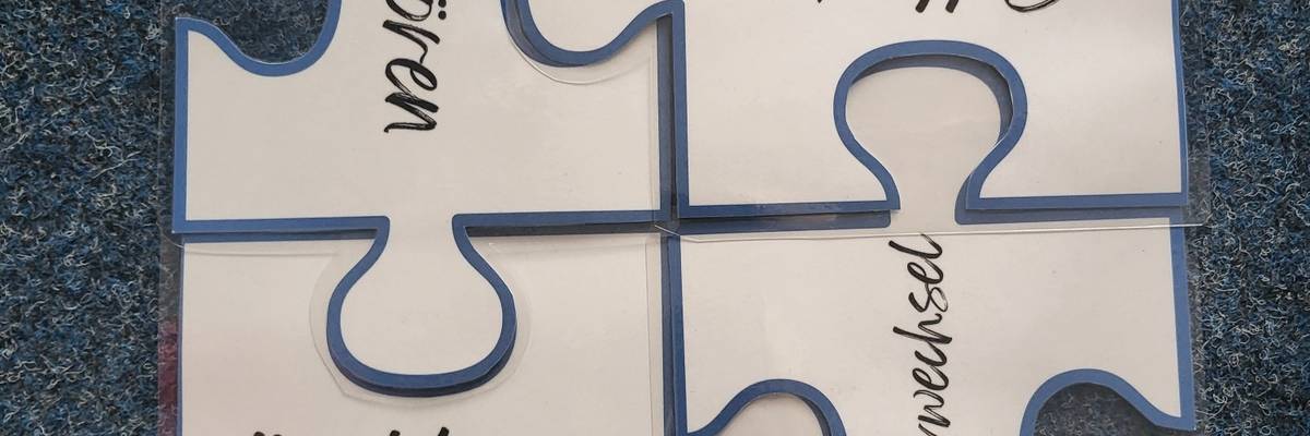 Ein weißes Puzzle bestehend aus vier Teilen mit Buchstaben.