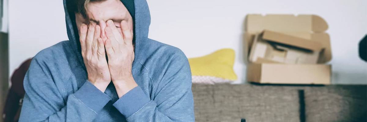 Jugendlicher mit übergezogener Kapuze und Hände vor dem Gesicht