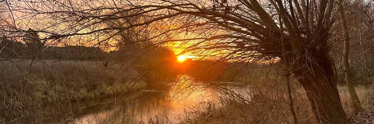 Orangefarbene Sonne und Nebel über einem Fluss.