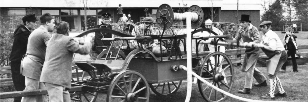 Männer bedienen historische Feuerwehrspritze auf Rasenplatz